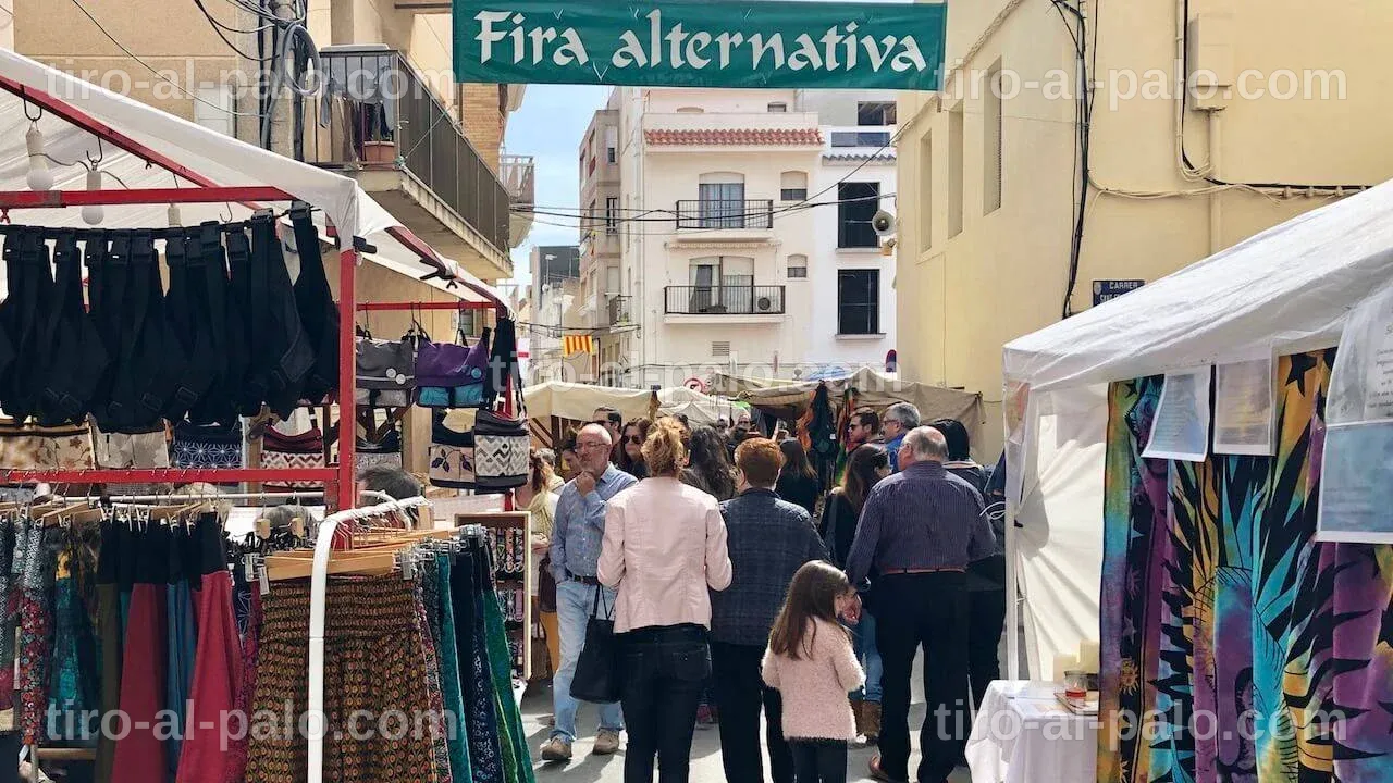 Familias explorando la Fira Alternativa de Ametlla de Mar con diversas atracciones.